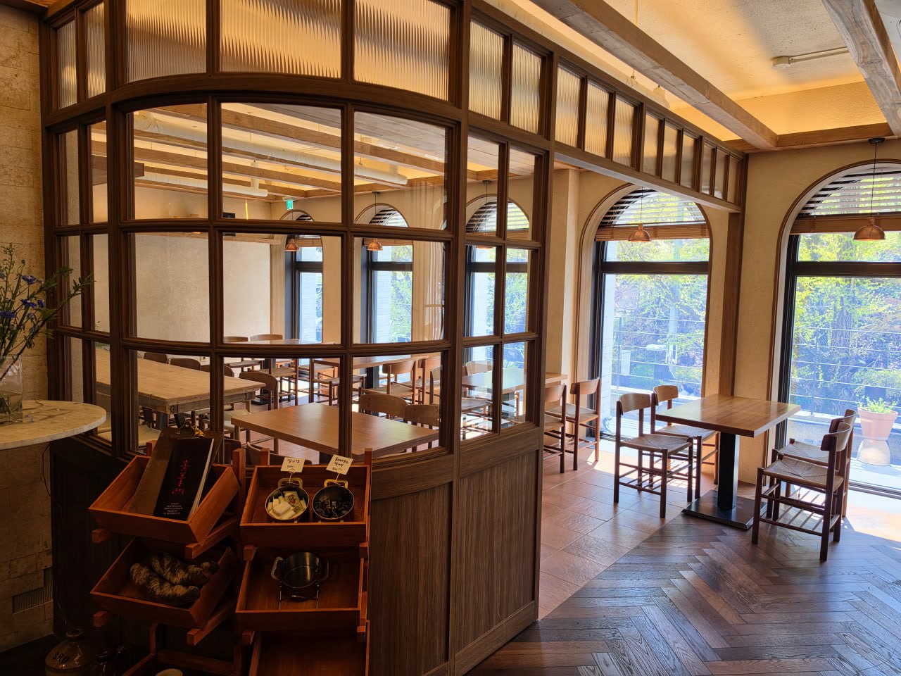 Warm dining room with wooden tables, arched windows, and a glass partition