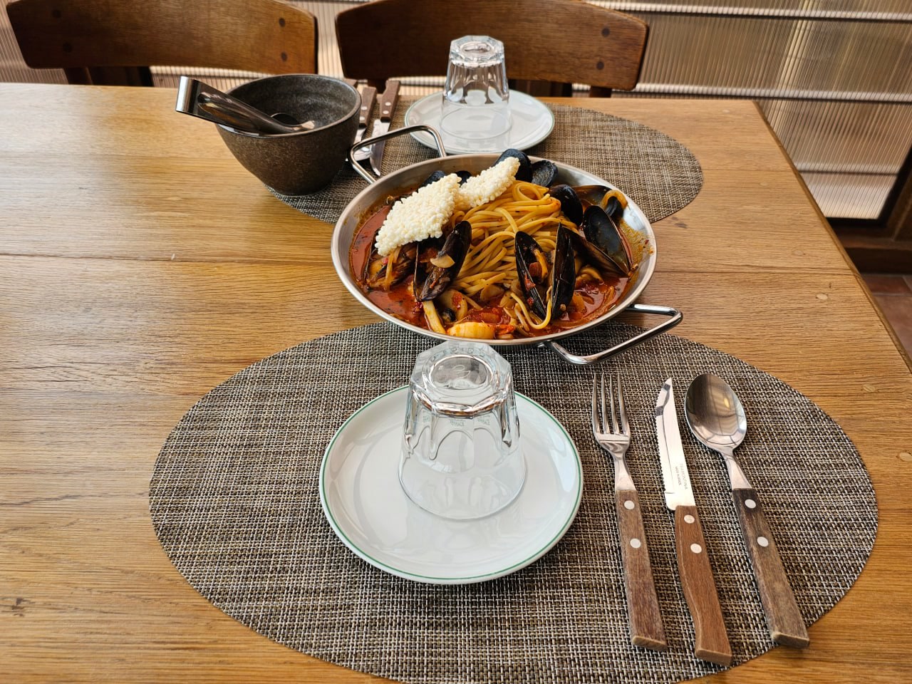 Pan of noodles with mussels and other seafood in red sauce on a set table